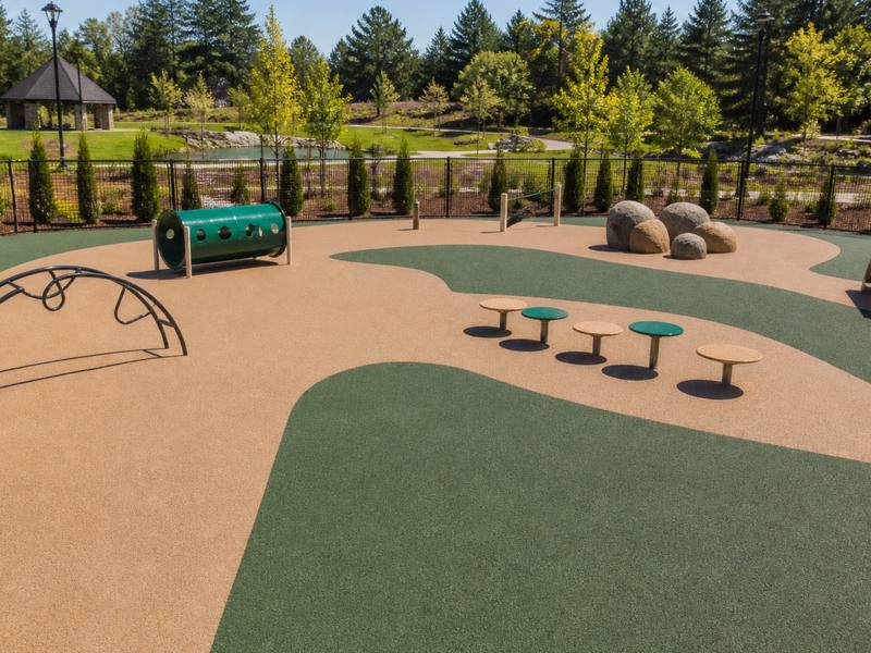 Fenced dog park with a tan rubber surfaced path and a green rubber play area