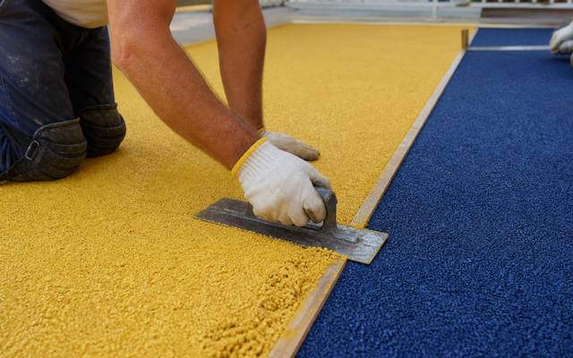 Installer troweling yellow rubber surfacing beside a blue section at a daycare