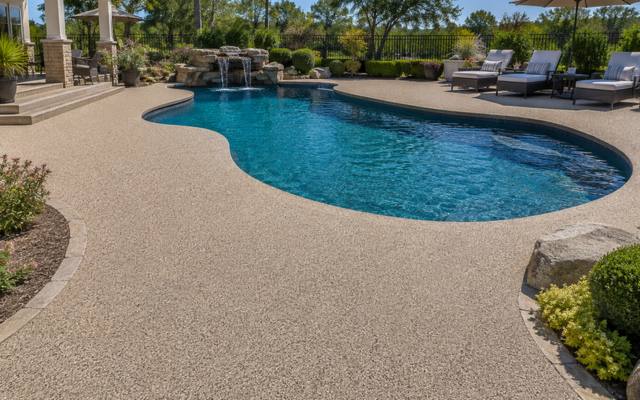 Backyard pool with a rock waterfall and a deck finished in sand-coloured rubber surfacing